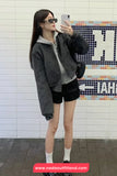 Person taking a mirror selfie wearing a dark jacket and black shorts against a tiled wall.