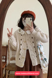 Person wearing a white cardigan with floral patterns, taking a mirror selfie.