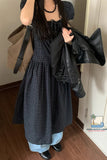 Person wearing a black and gray checkered dress with a black jacket, holding bags indoors.
