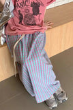 Person wearing a pink shirt with a graphic design and plaid pants sitting on a wooden bench.