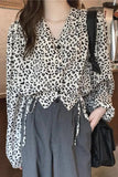 Person wearing a leopard print blouse and gray pants, holding a black bag.