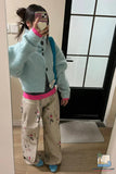 Person wearing a light blue cardigan, pink shirt, floral pants, and blue shoes in front of a mirror.