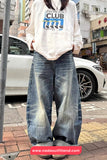 Person wearing a white sweatshirt with graphic design and blue jeans on a street.