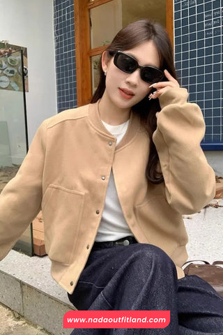 Woman wearing a beige jacket and sunglasses, sitting on steps with a building in the background.