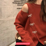 Red sweater with bow details worn by a person, against a textured wall background.