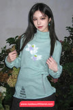 Woman wearing a light blue sweater with floral design against a blurred natural background