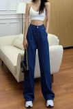 Person wearing a white crop top and blue pleated pants standing in a living room.