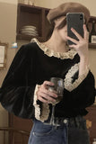 Person wearing a black sweater with lace details, holding a glass of wine and taking a selfie.