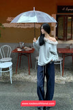 Woman holding a transparent umbrella in an outdoor setting with tables and chairs.