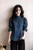 Woman wearing a blue denim blouse with gold buttons against a plain background