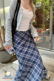 Person wearing a white top and blue plaid skirt in an outdoor setting.