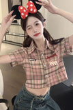 Person wearing a plaid shirt with red accents and denim pants, posing indoors.