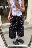 Person wearing a white sleeveless top with cartoon designs and black polka dot pants, standing in front of a mirror.