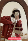 Person wearing a red cardigan and white hat, holding a phone, with a beige bag featuring floral details.