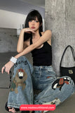 Woman wearing a black top and jeans with dog designs, sitting against a concrete wall.