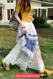 Person wearing a yellow top and white skirt with blue accents outdoors.