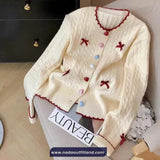 White cardigan with decorative bows and buttons on a chair, branded 'Nada Outfit Land'.