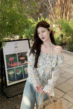 Woman in a floral off-shoulder top standing outdoors with greenery in the background