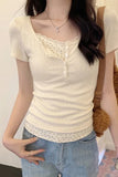 Woman wearing a light-colored top with lace details and blue jeans, standing against a plain background.