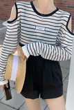 Person wearing a black and white striped long-sleeve top and black shorts, holding a straw bag.