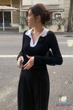 Woman in a black outfit with white collar standing on a street.