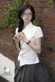 Woman wearing a white blouse and dark skirt against a brick wall.