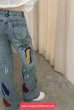 Person wearing blue jeans with colorful paint designs indoors.