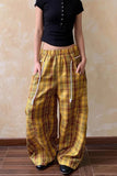 Person wearing yellow plaid pants with a black top against a beige wall.