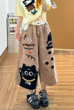 Person wearing a yellow shirt with cartoon designs and brown pants with black cat illustrations on a wooden floor.