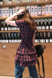 Person wearing a plaid dress in front of a shelf with bottles