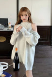 Woman in a white ribbed sweater standing in an indoor setting with a bottle of wine on a table.