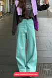 Person wearing teal pants and a black jacket with a purple shirt, standing on a sidewalk.