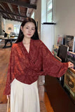 Woman wearing a red patterned blouse and white pants in an indoor setting.