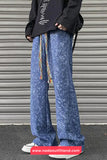 Person wearing blue patterned pants and a black jacket with text, standing against a metallic shutter.