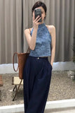 Woman taking a mirror selfie wearing a blue top and dark pants, holding a woven bag.