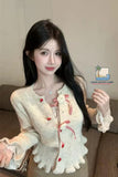 Woman wearing a light-colored outfit with decorative elements, sitting on a couch.