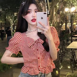 Woman taking a selfie in a red and white checkered top outdoors at night.