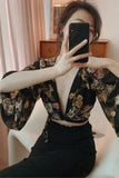Person wearing a floral top and black pants sitting on a white chair.