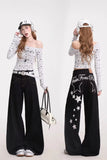 Woman wearing a white off-shoulder top with star patterns and black wide-leg pants, posing against a white background.