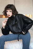 Person wearing a black leather jacket and blue jeans sitting indoors.