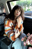 Woman sitting in a car holding pink flowers, wearing a colorful striped sweater.