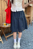 Person wearing a white shirt, blue plaid skirt, and white sneakers outdoors.