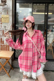 Person wearing a pink checkered shirt and cap in front of a store entrance.
