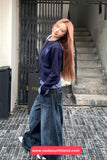 Person wearing a navy sweater and wide-leg jeans standing on a street with a staircase in the background.