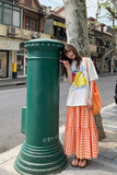 Woman standing next to a green postbox on a city street