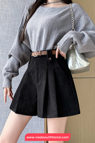 Person wearing a gray sweater and black skirt with a neutral background