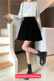 Person wearing a white sweater, black skirt, and black boots standing on a staircase.