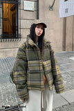 Person wearing a plaid jacket and cap standing on a street.