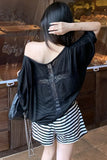 A woman shown from behind wearing a black one-shoulder satin top with lace detailing and black-and-white striped shorts, standing in front of a wooden display case.