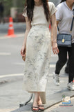 Woman wearing a beige top and floral skirt on a street.